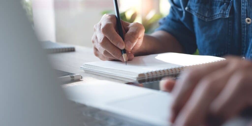 Efficient business planning and note-taking with a person writing in a notebook, symbolizing organization and productivity in a professional work environment.